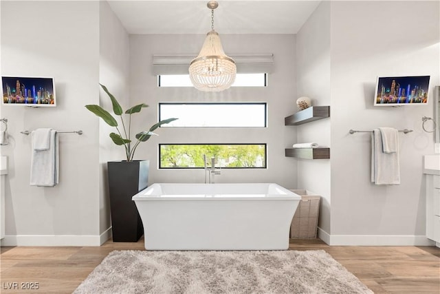 bathroom with an inviting chandelier, baseboards, a soaking tub, and wood finished floors