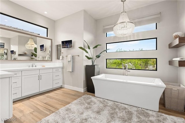 bathroom featuring vanity, wood finished floors, a wealth of natural light, a soaking tub, and a notable chandelier