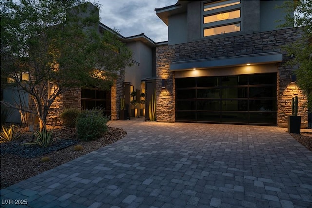 modern home with decorative driveway, stone siding, and stucco siding