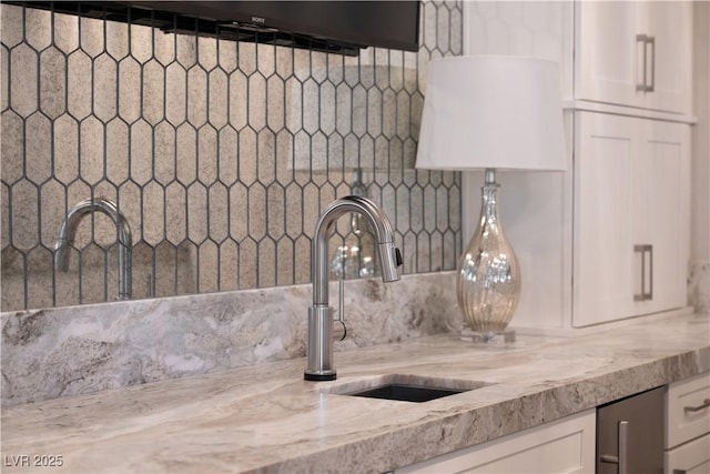 interior details with backsplash, white cabinetry, light stone counters, and a sink