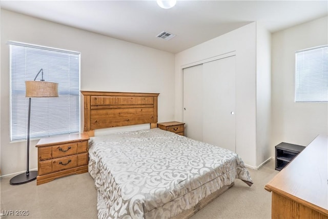 bedroom with a closet, baseboards, light colored carpet, and visible vents