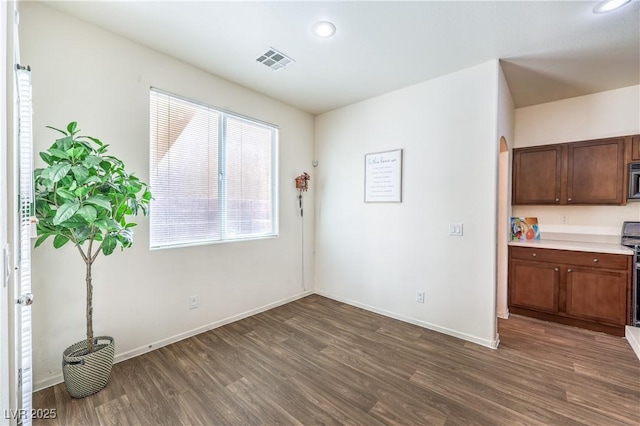 unfurnished dining area with visible vents, baseboards, dark wood-type flooring, recessed lighting, and arched walkways