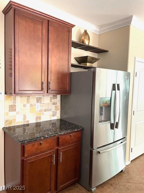 kitchen with tasteful backsplash, light tile patterned floors, stainless steel fridge with ice dispenser, dark stone counters, and ornamental molding