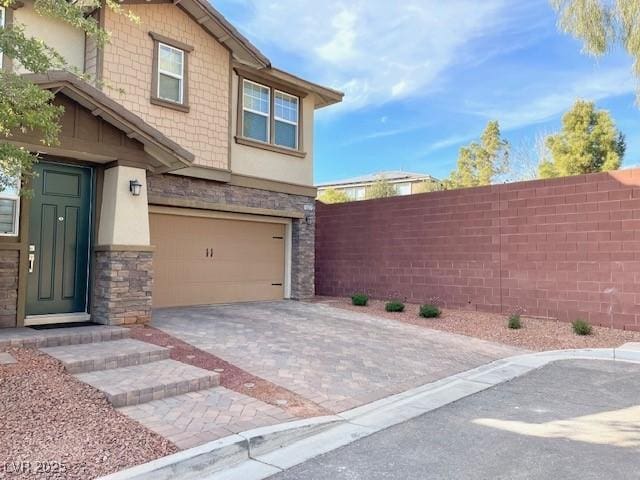 view of home's exterior with fence, an attached garage, stone siding, stucco siding, and decorative driveway