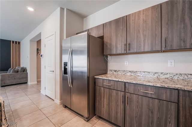kitchen featuring open floor plan, light tile patterned floors, light stone countertops, and stainless steel fridge with ice dispenser