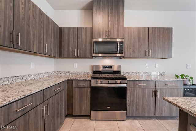 kitchen with light tile patterned floors, appliances with stainless steel finishes, dark brown cabinetry, and light stone counters