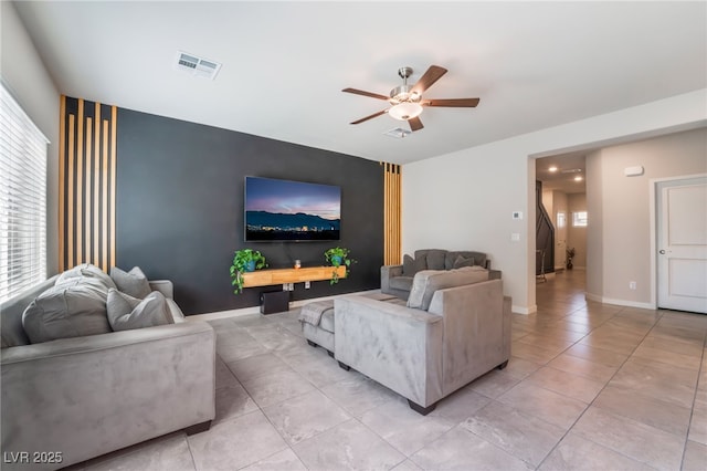 living room featuring a ceiling fan, visible vents, baseboards, an accent wall, and light tile patterned flooring