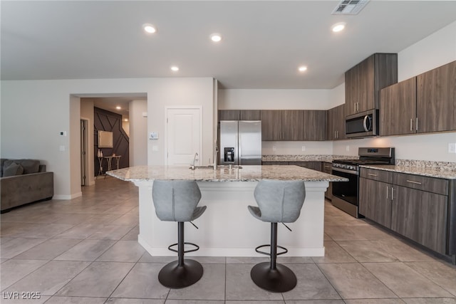 kitchen with visible vents, a breakfast bar area, an island with sink, light tile patterned floors, and stainless steel appliances