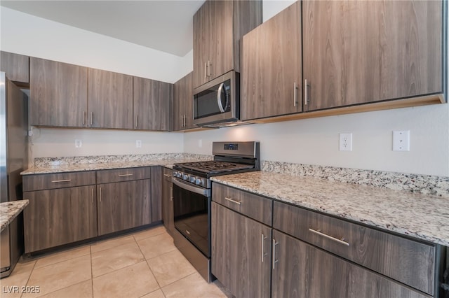 kitchen with light tile patterned flooring, dark brown cabinetry, appliances with stainless steel finishes, and light stone counters
