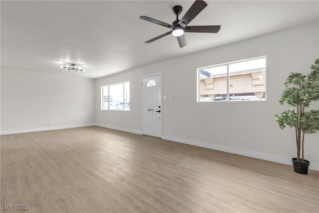 unfurnished living room featuring baseboards, ceiling fan with notable chandelier, and light wood finished floors