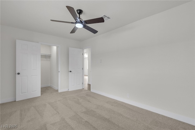 unfurnished bedroom with visible vents, light carpet, baseboards, a walk in closet, and ceiling fan