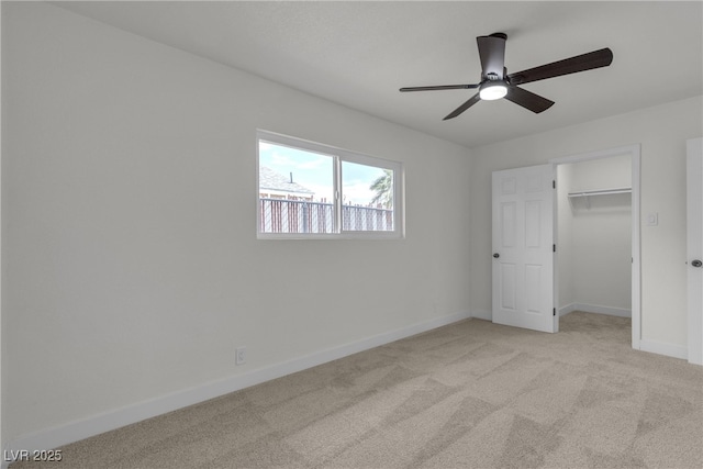 unfurnished bedroom featuring a closet, baseboards, ceiling fan, a walk in closet, and carpet