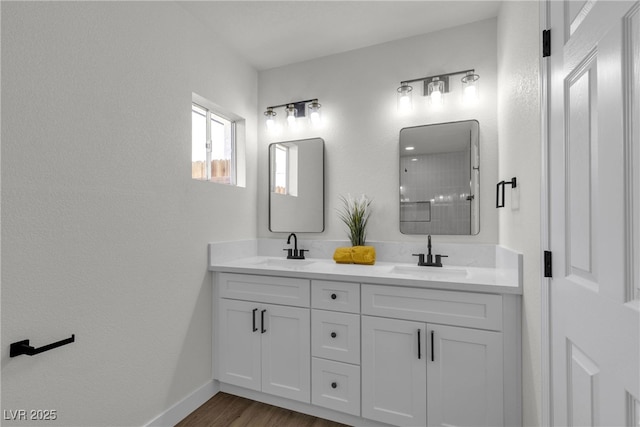 full bath featuring a sink, baseboards, double vanity, and wood finished floors