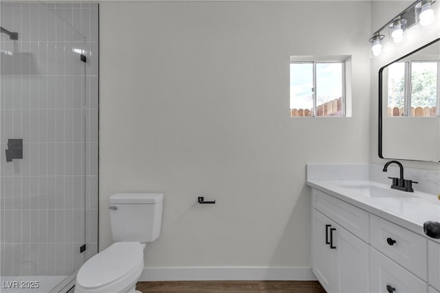 full bathroom with toilet, baseboards, tiled shower, and vanity