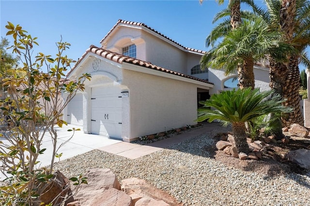view of side of property with a garage, stucco siding, driveway, and a tile roof