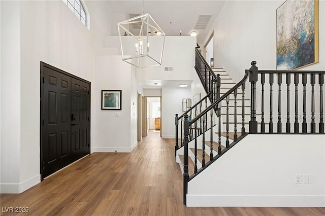 foyer entrance featuring baseboards, a high ceiling, visible vents, and wood finished floors