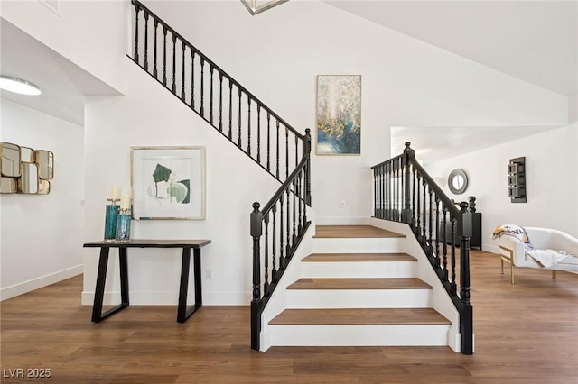 stairway featuring high vaulted ceiling, baseboards, and wood finished floors