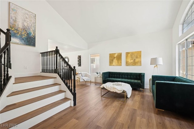 living room with stairs, high vaulted ceiling, and wood finished floors