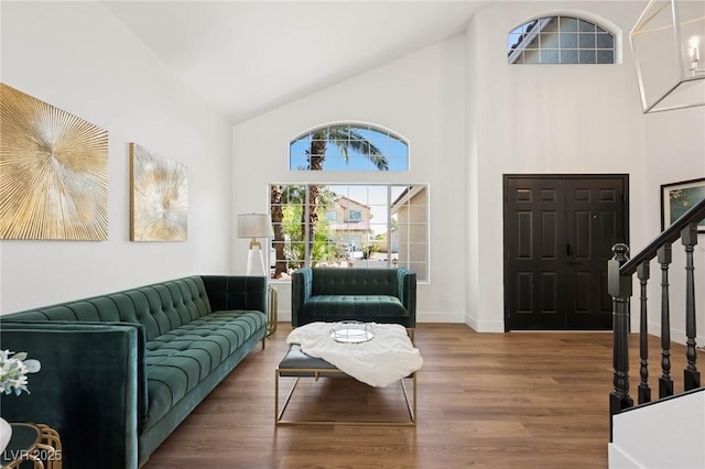 living area with a healthy amount of sunlight, high vaulted ceiling, stairs, and wood finished floors