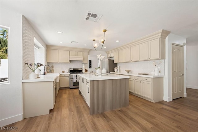 kitchen featuring decorative backsplash, light wood-style floors, light countertops, under cabinet range hood, and stainless steel appliances