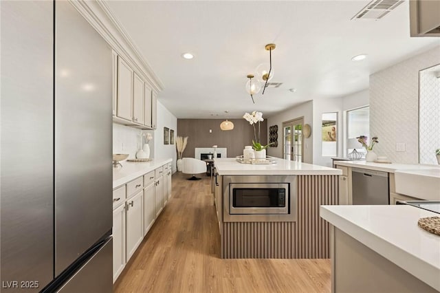 kitchen with hanging light fixtures, appliances with stainless steel finishes, light wood-style floors, light countertops, and visible vents