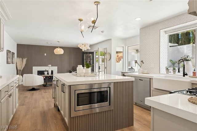 kitchen with appliances with stainless steel finishes, a sink, light countertops, an accent wall, and light wood-type flooring