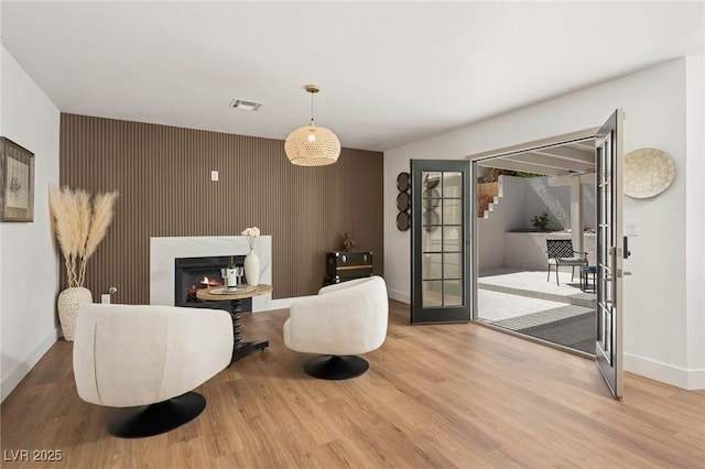 living room featuring a lit fireplace, visible vents, wood finished floors, baseboards, and an accent wall