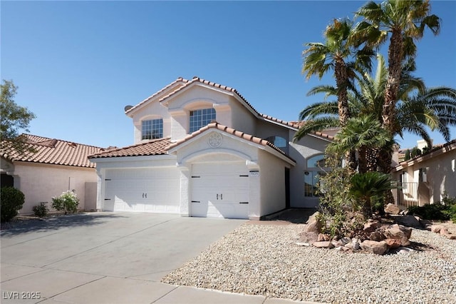 mediterranean / spanish home with an attached garage, driveway, a tile roof, and stucco siding