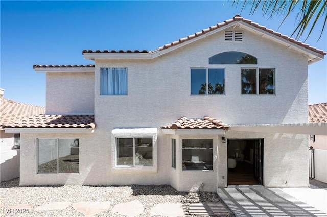 rear view of property featuring a tile roof and stucco siding