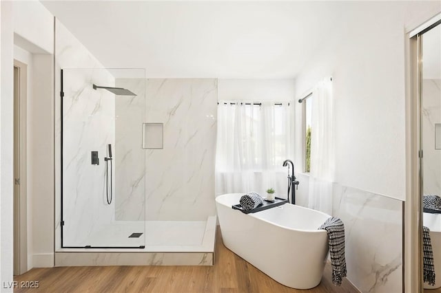 full bath featuring a freestanding bath, a marble finish shower, and wood finished floors