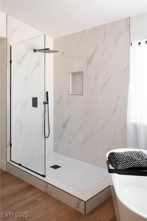bathroom with a freestanding bath, a marble finish shower, and wood finished floors