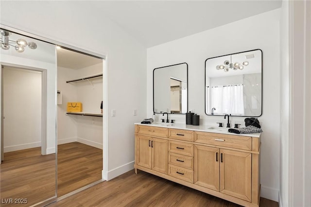 full bath with double vanity, a sink, baseboards, and wood finished floors