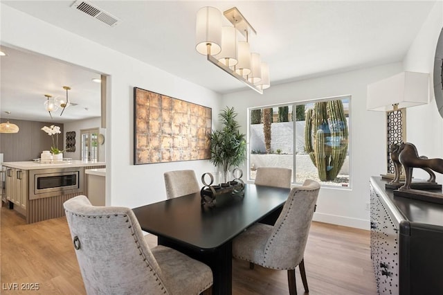 dining space with a notable chandelier, baseboards, visible vents, and light wood-style floors