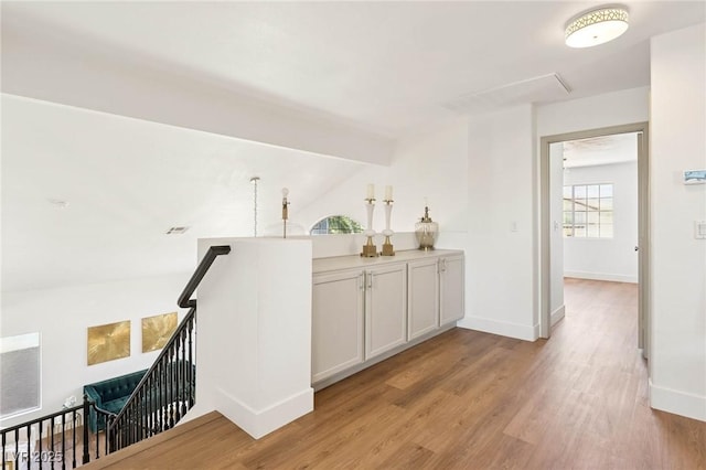 corridor with baseboards, an upstairs landing, lofted ceiling, and light wood finished floors