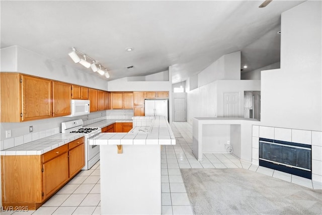 kitchen featuring white appliances, tile countertops, vaulted ceiling, and light tile patterned flooring