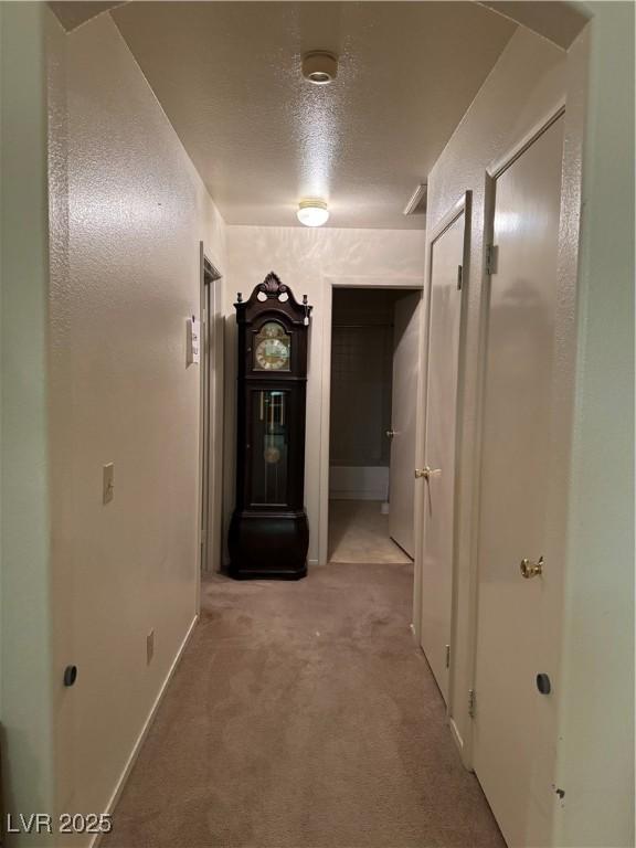hall with carpet, a textured ceiling, and baseboards
