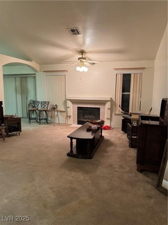 living area with arched walkways, ceiling fan, a fireplace, and carpet flooring