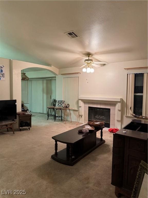 living area with ceiling fan, arched walkways, a fireplace, and carpet
