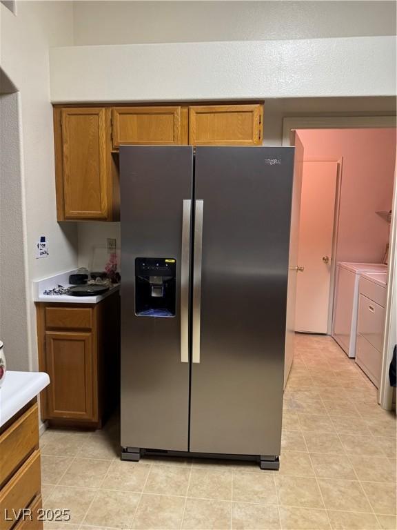 kitchen with stainless steel fridge with ice dispenser, washing machine and clothes dryer, brown cabinets, light countertops, and light tile patterned flooring