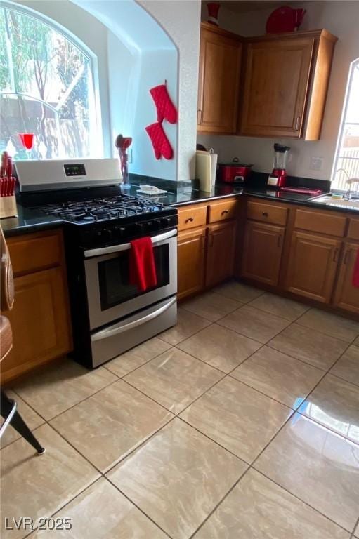11021 Pentland Downs St, Las Vegas, NV 89141 - kitchen with stainless steel gas range, light tile patterned flooring, dark countertops, and a sink