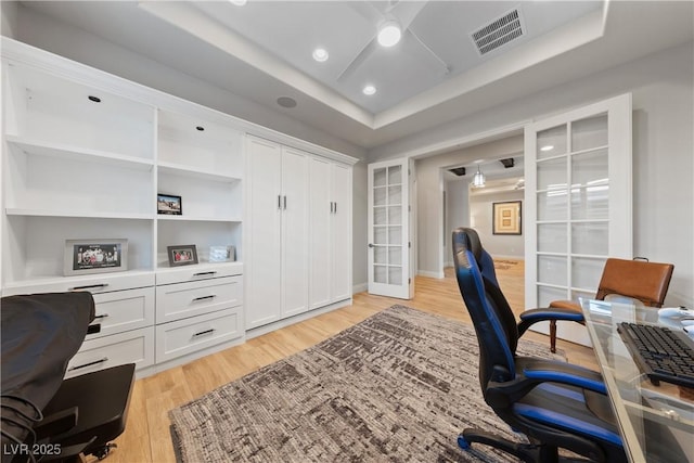 home office featuring light wood-style floors, french doors, a ceiling fan, a tray ceiling, and visible vents