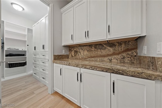 interior space featuring light wood-type flooring, white cabinetry, dark stone countertops, and tasteful backsplash