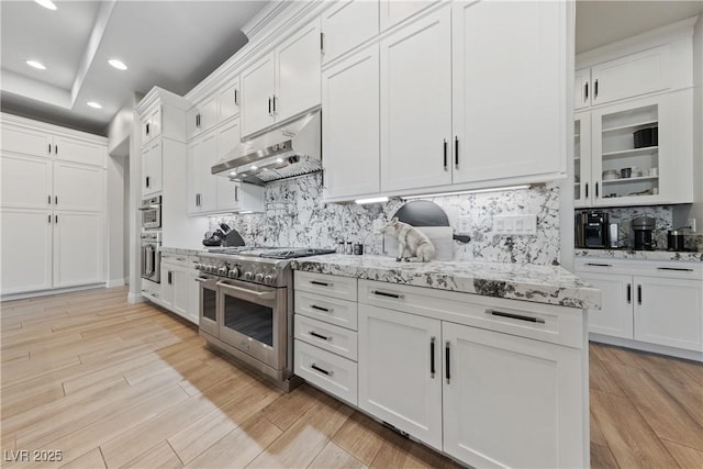 kitchen with under cabinet range hood, stainless steel appliances, white cabinets, and tasteful backsplash