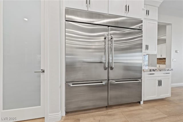 kitchen featuring white cabinetry, built in refrigerator, light stone countertops, and light wood finished floors