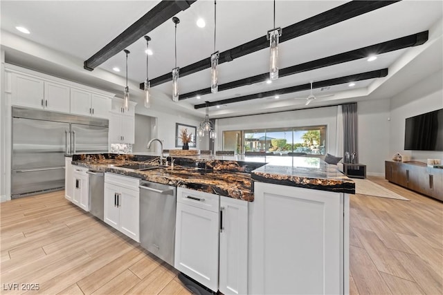 kitchen featuring a sink, light wood-style flooring, stainless steel appliances, open floor plan, and beamed ceiling