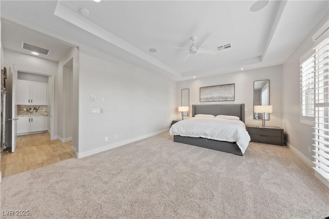 bedroom featuring light colored carpet, a raised ceiling, baseboards, and visible vents