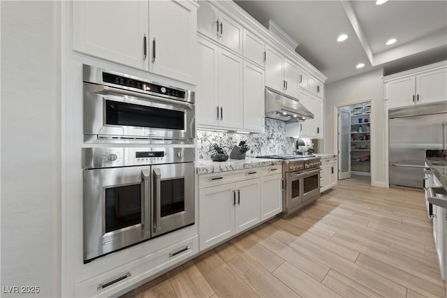 kitchen featuring recessed lighting, white cabinetry, under cabinet range hood, backsplash, and premium appliances