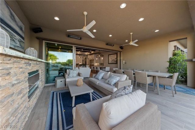 living area with an outdoor stone fireplace, a ceiling fan, and recessed lighting