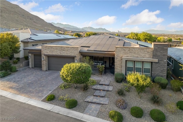 view of front of home with a mountain view, roof mounted solar panels, stone siding, and a garage