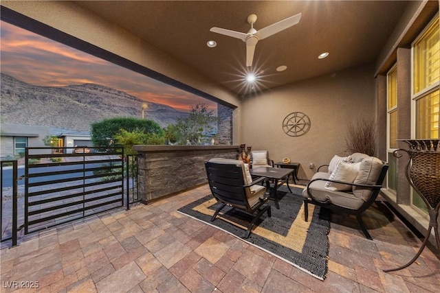 patio terrace at dusk featuring a gate, a ceiling fan, and a mountain view